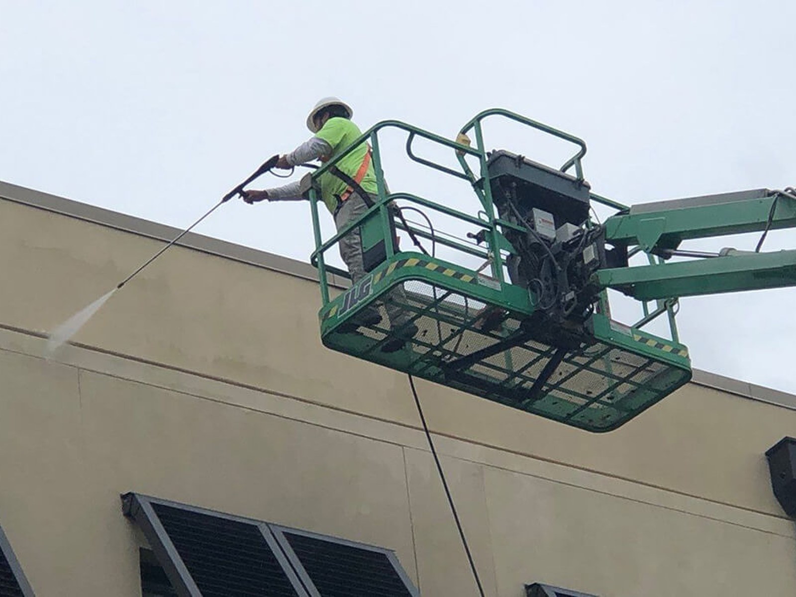 Technician pressure washing a commercial facade from a boom lift